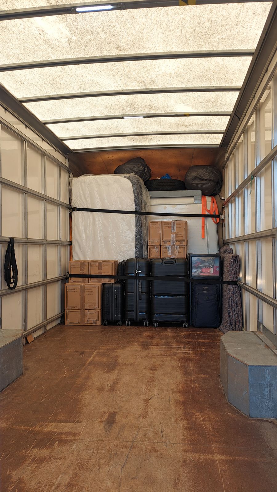 Van interior with a wrapped mattress, boxes and suitcases strapped in place